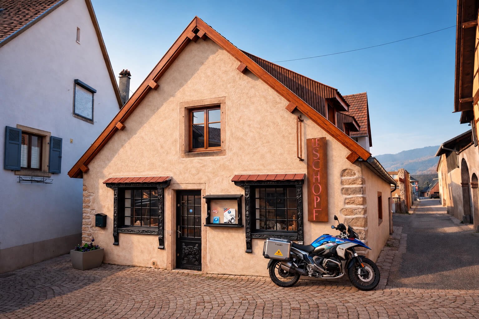 Die Fassade des „Schopf“, eines Steinhauses an der Ecke einer gepflasterten Straße in Ottrott, davor steht ein Motorrad